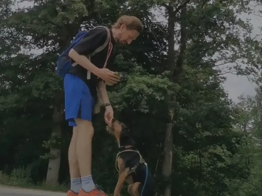 Fabian gibt Terrier-Mix Törpi auf einem Waldweg ein Signal